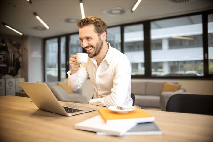 smiling man at a table with laptop holding cup